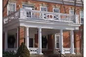 Brick two-story building entrance with a covered front porch supported by white columns and a decorative white balcony railing above.