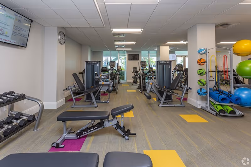 Well-lit fitness center with weight benches, strength machines, dumbbells and exercise balls.