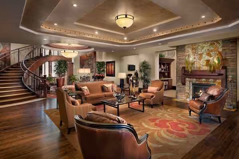 Luxurious lobby lounge with leather seating, warm fireplace, and curved staircase on the left.