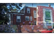 Exterior brick building with mural on the lower wall and a parked red car.