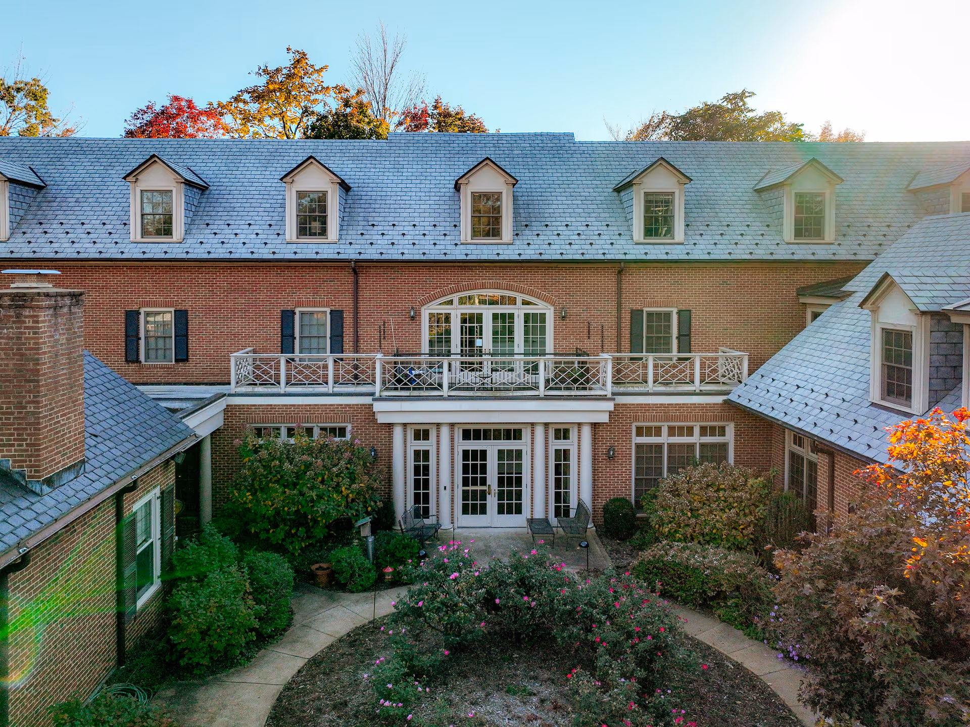 Front view of a two-story brick building with dormer windows, a central balcony, and a landscaped courtyard.