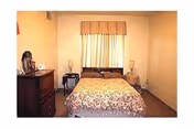 Cozy bedroom with a double bed under a curtained window, floral bedding, two nightstands with lamps and a dresser.