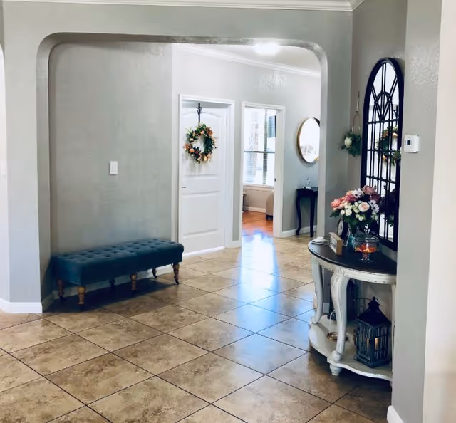Bright tiled foyer with a teal bench on the left and a decorative console table with flowers and mirror on the right, leading to interior rooms.