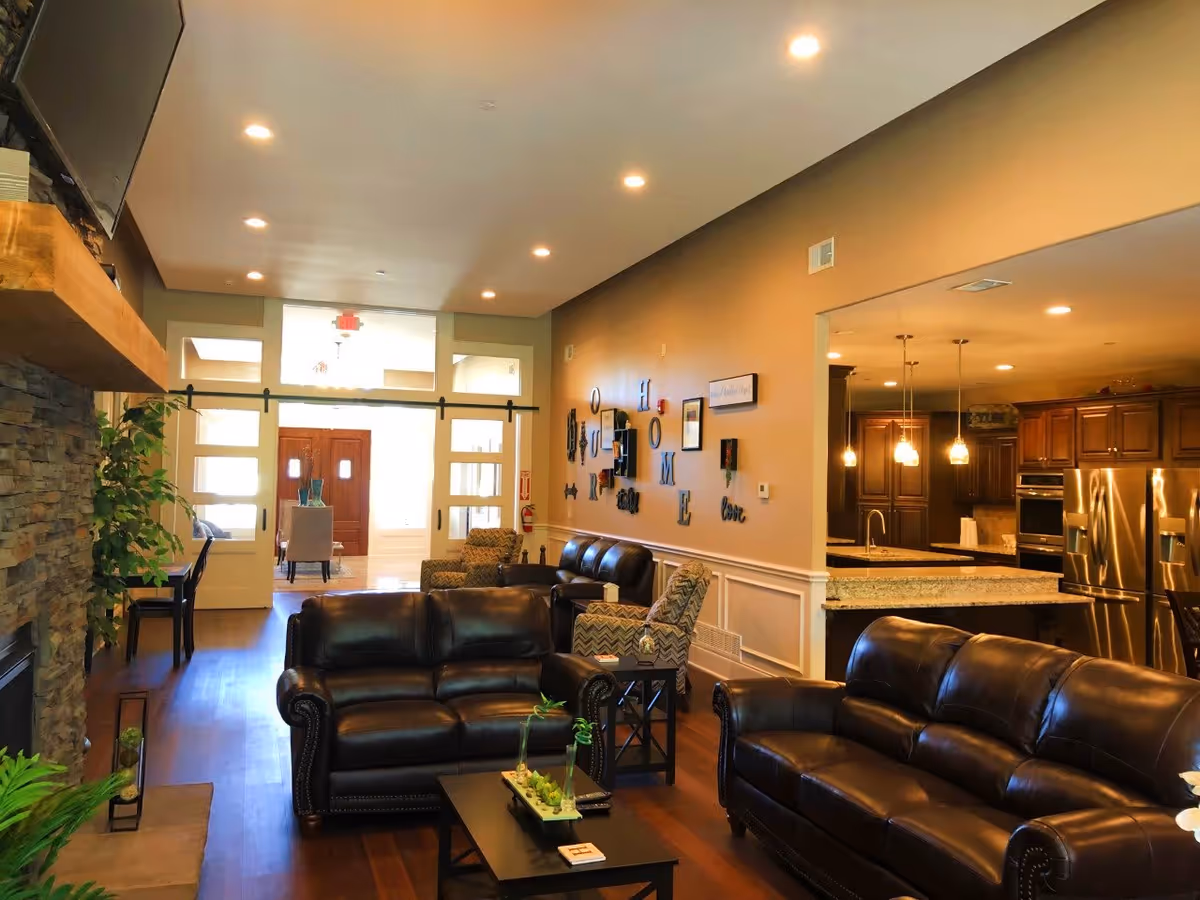 Spacious open living room with leather sofas, a coffee table, stone fireplace, and a view into the kitchen and entryway.
