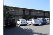 Parking lot in front of a two-story residential building with multiple doors and windows, under a clear blue sky.