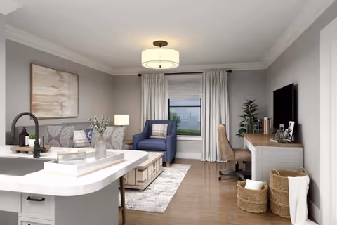 A modern living room with a gray sofa, a blue armchair, a wooden coffee table on a light rug, and a desk with a chair and a TV mounted on the wall. The room has light gray walls, a window with white curtains, and a ceiling light fixture. There are decorative items including a plant, books, and baskets.