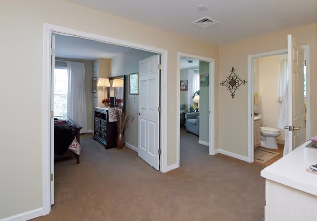 Carpeted apartment interior with open doorways leading to a bedroom, a sitting area, and a bathroom.