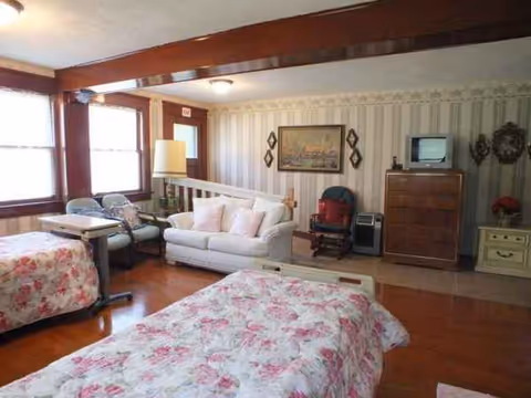 Two floral beds in a senior home bedroom with sofa, dresser, and TV.