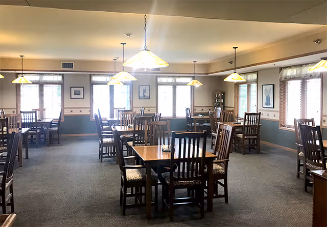 Spacious dining room with multiple wooden tables and chairs, pendant lights, and large windows.