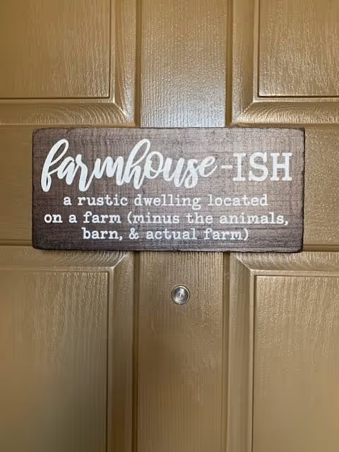 A wooden sign hanging on a brown door that reads: 'farmhouse-ISH a rustic dwelling located on a farm (minus the animals, barn, & actual farm)'