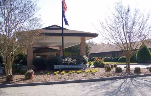 Front view of The Hamilton Assisted Living entrance with flagpole and landscaped surroundings.