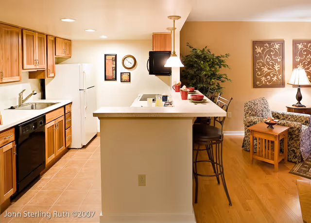Open-plan kitchen with a breakfast bar and stools opening into a cozy living area with chairs and wall art.