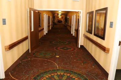 A long, carpeted hallway in a senior living facility with framed pictures along walls.