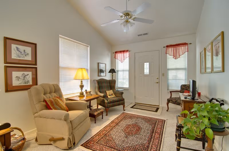 Cozy living room with a recliner and wingback chair, patterned area rug, side tables with lamps, and a front door with windows.