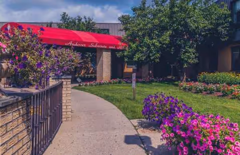 Path to a brick building entrance, red canopy, and vibrant flowers along the walkway.