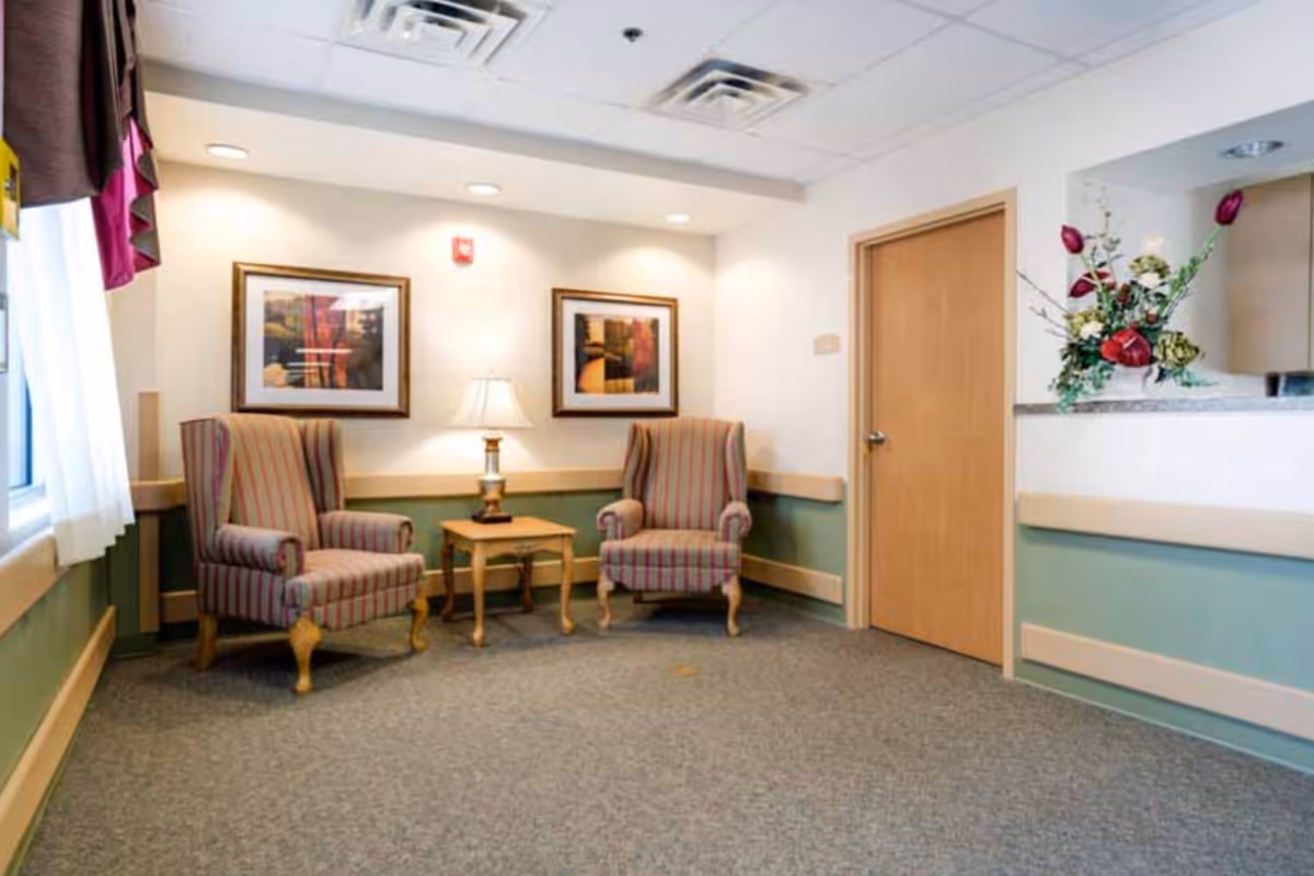 Small reception/waiting area with two striped armchairs, a side table and lamp, framed artwork on the wall, and a reception counter with a floral arrangement.