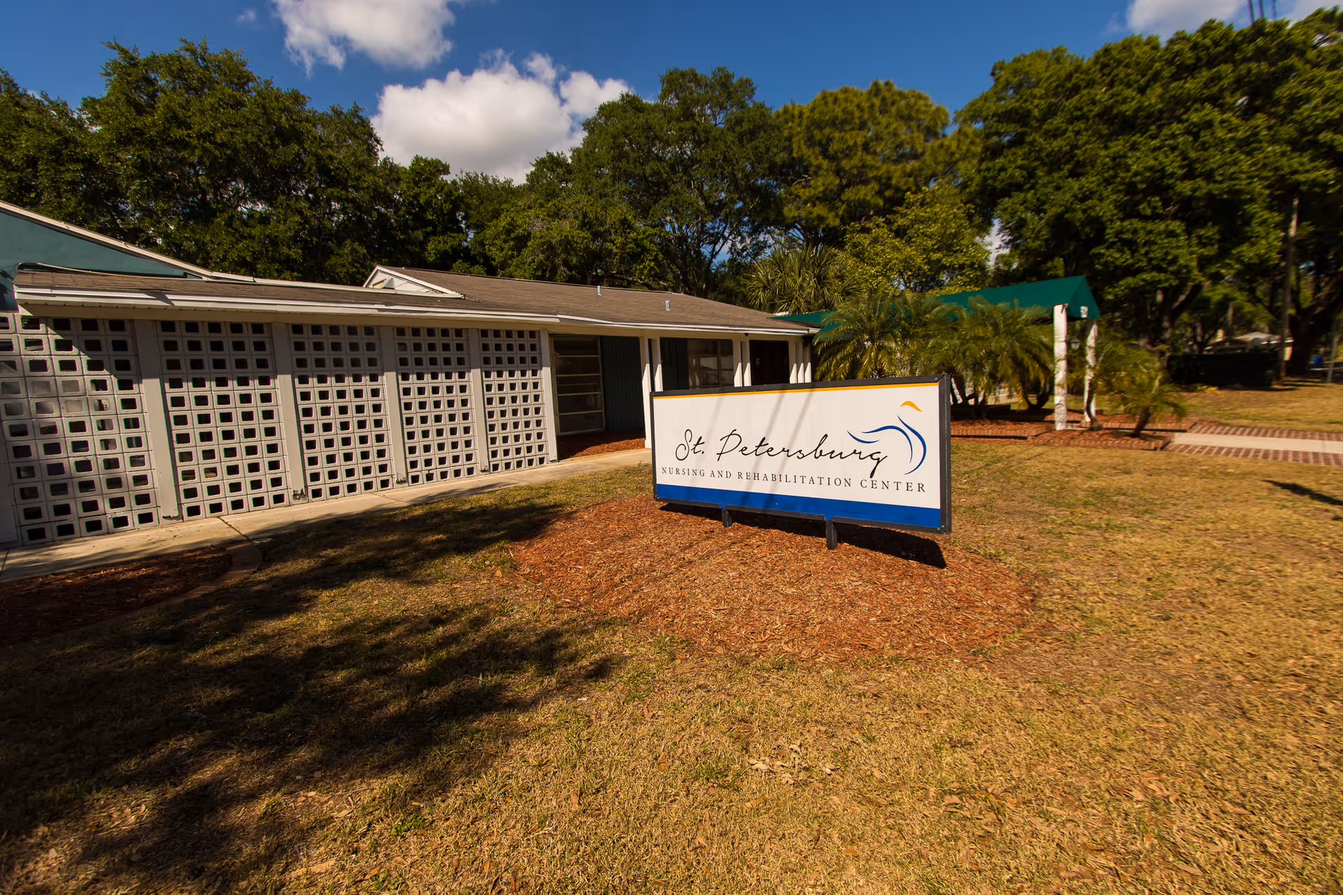 Freestanding sign reading 'St. Petersburg Nursing and Rehabilitation Center' on a grassy lawn in front of a low building and trees.