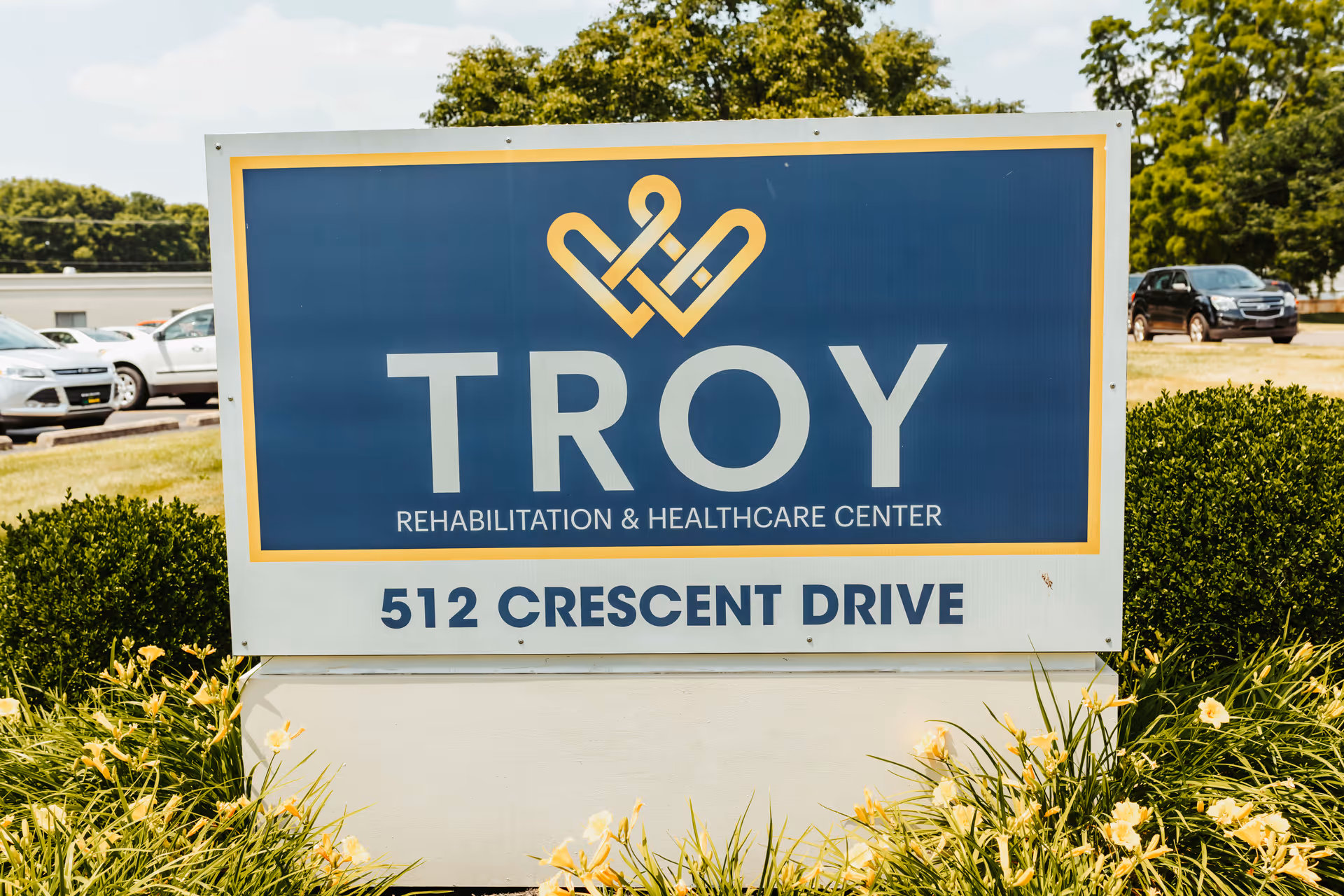 Large outdoor sign for Troy Rehabilitation & Healthcare Center displaying the address 512 Crescent Drive surrounded by landscaping.