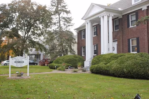 Brick building with white columns and manicured shrubs in front of Hazel L. Carpenter Adult Home.