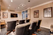 Small media lounge with rows of black reclining chairs facing a wall-mounted TV and framed artwork on the walls.