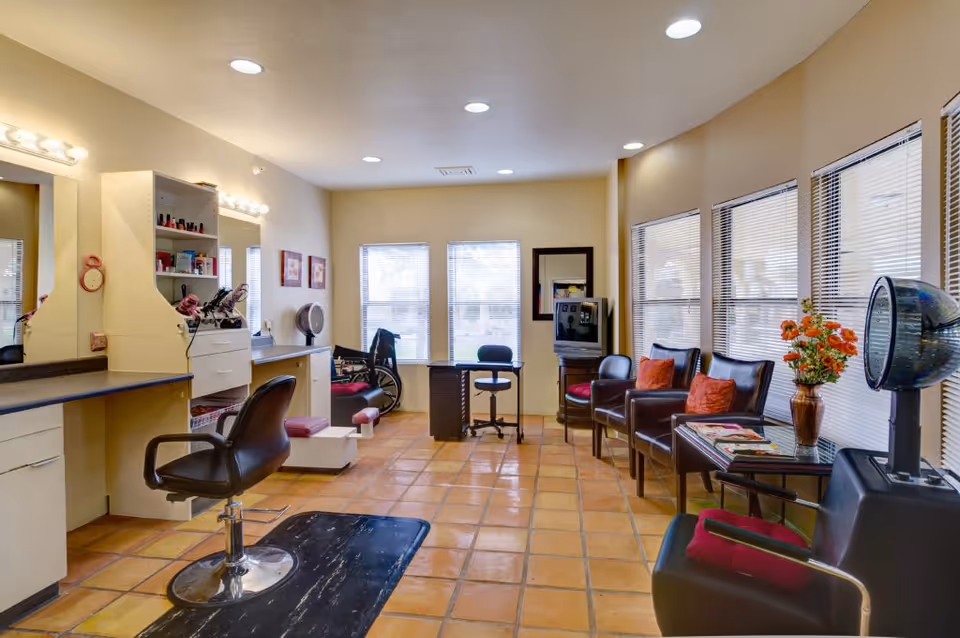 Interior salon area with styling chairs, mirrors, a hooded hair dryer, and seating along windows.