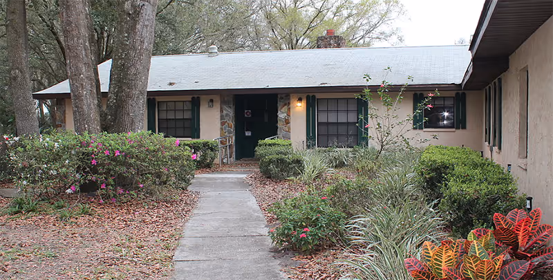 Exterior view of a single-story senior living facility with a walkway and landscaped garden.