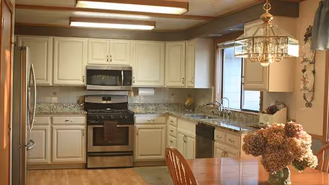 White kitchen with stainless steel appliances, white cabinets, and a wooden dining table.