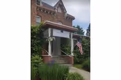 Brick building entrance with small porch, stairs, and an American flag.