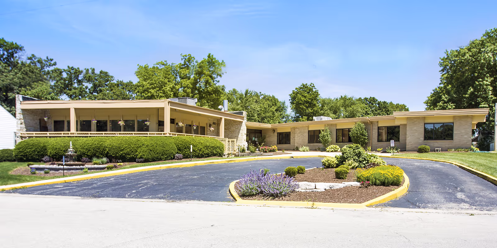 Exterior view of a single-story senior living facility with a circular driveway and landscaped front area.