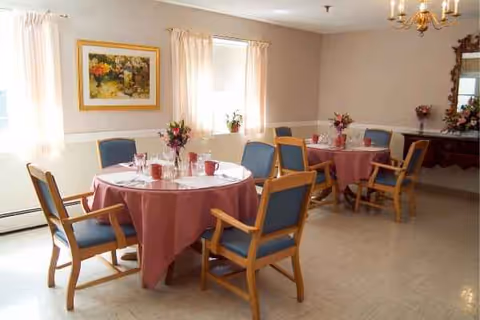 Bright dining room with pink tablecloths, floral centerpieces, and empty chairs in a senior facility.