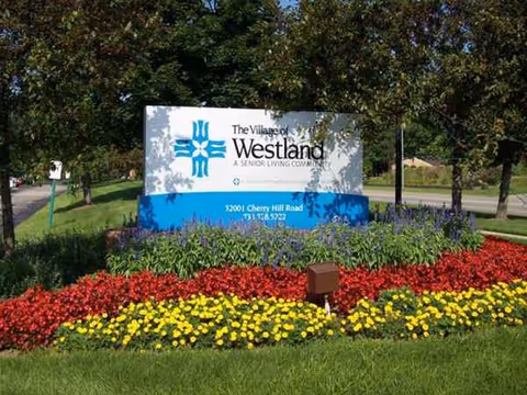 Colorful flower beds frame a sign for The Village of Westland senior living.