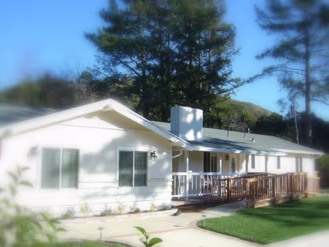 White single-story retirement facility with a wooden front porch and manicured lawn.