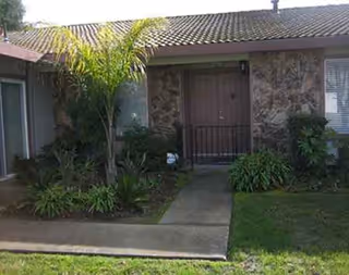 Front exterior of a senior living facility entry with stone facade and landscaping.