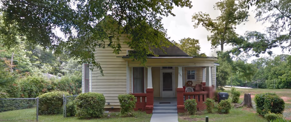 A small, single-story house with a front porch, path, and green yard.