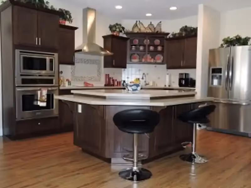 Modern kitchen with a central island, two bar stools, stainless steel appliances and dark wood cabinets.