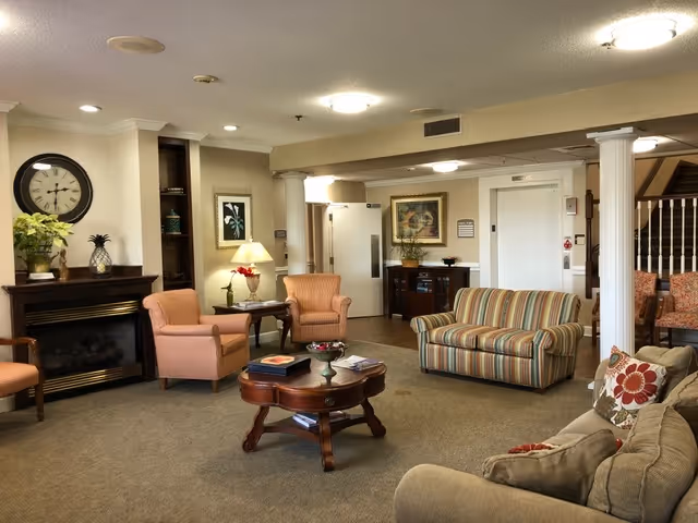 Comfortable senior living common lounge with sofas, upholstered chairs, a fireplace, and a central coffee table.