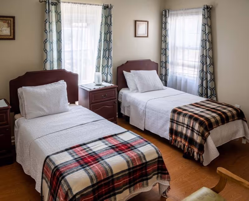 Two twin beds with plaid blankets in a cozy bedroom suite with windows.