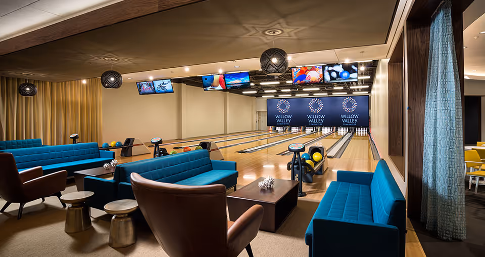 Interior bowling alley with teal sofas and leather armchairs facing multiple lanes and 'Willow Valley' signage.