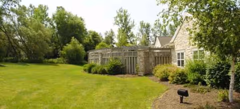 Lush green lawn surrounds a low, stone-clad building exterior with windows.