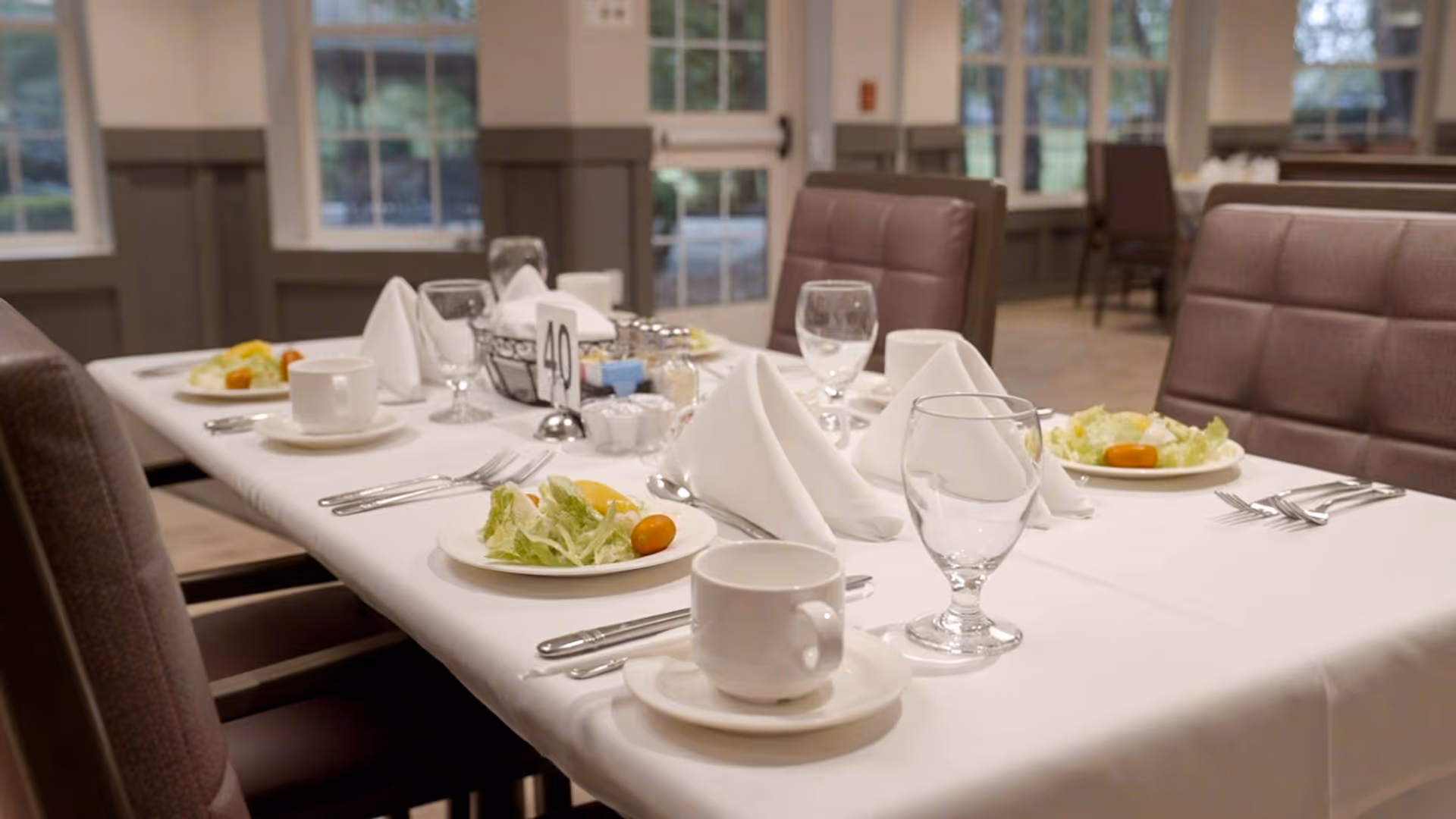 A formally set dining table with plates of salad, glassware, cups and folded napkins in a dining room.