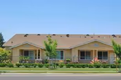 Front exterior of a single-story beige apartment building with covered porches, landscaping, and a street in front.