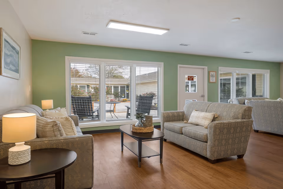 Bright living room lounge with sofas, coffee tables, and large windows overlooking a patio.