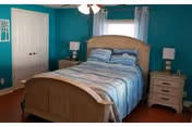 A bedroom with a wooden bed dressed in blue-striped bedding, teal painted walls, two matching nightstands with lamps, and a curtained window.