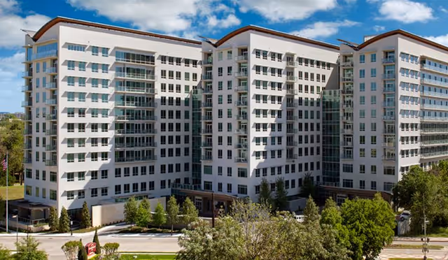 Front exterior of a large multi-story white senior living building with many windows and landscaped grounds.