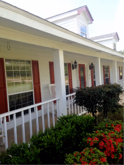 Front view of a white senior living building with red shutters and a covered porch.