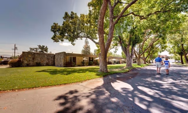 Exterior view of Piners Guest Home with trees along a street; two people walking away.