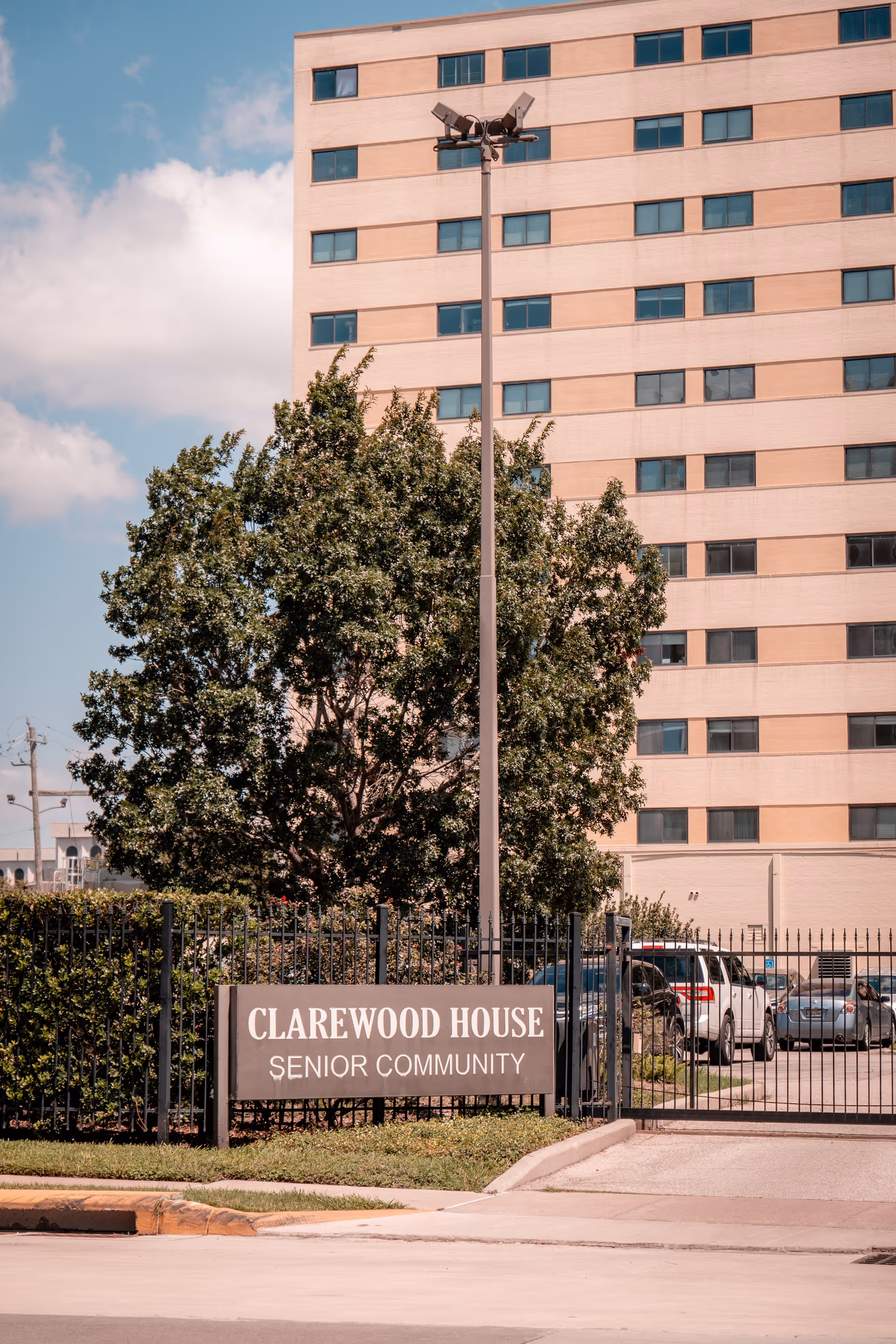 Exterior view of a multi-story senior living building with a gated entrance and a sign reading 'Clarewood House Senior Community'.
