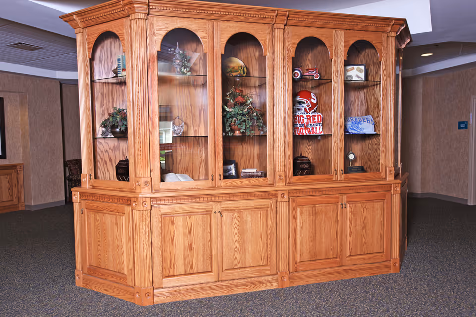 Large wooden glass-front display cabinet with decorative items in a facility interior.