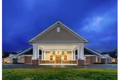 Front view of a lit senior living facility entrance with columns and brick exterior.
