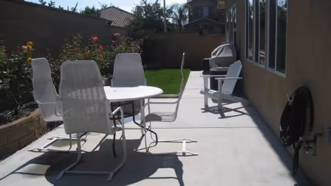 Outdoor concrete patio with a white table, chairs, and lounge seating beside the building.